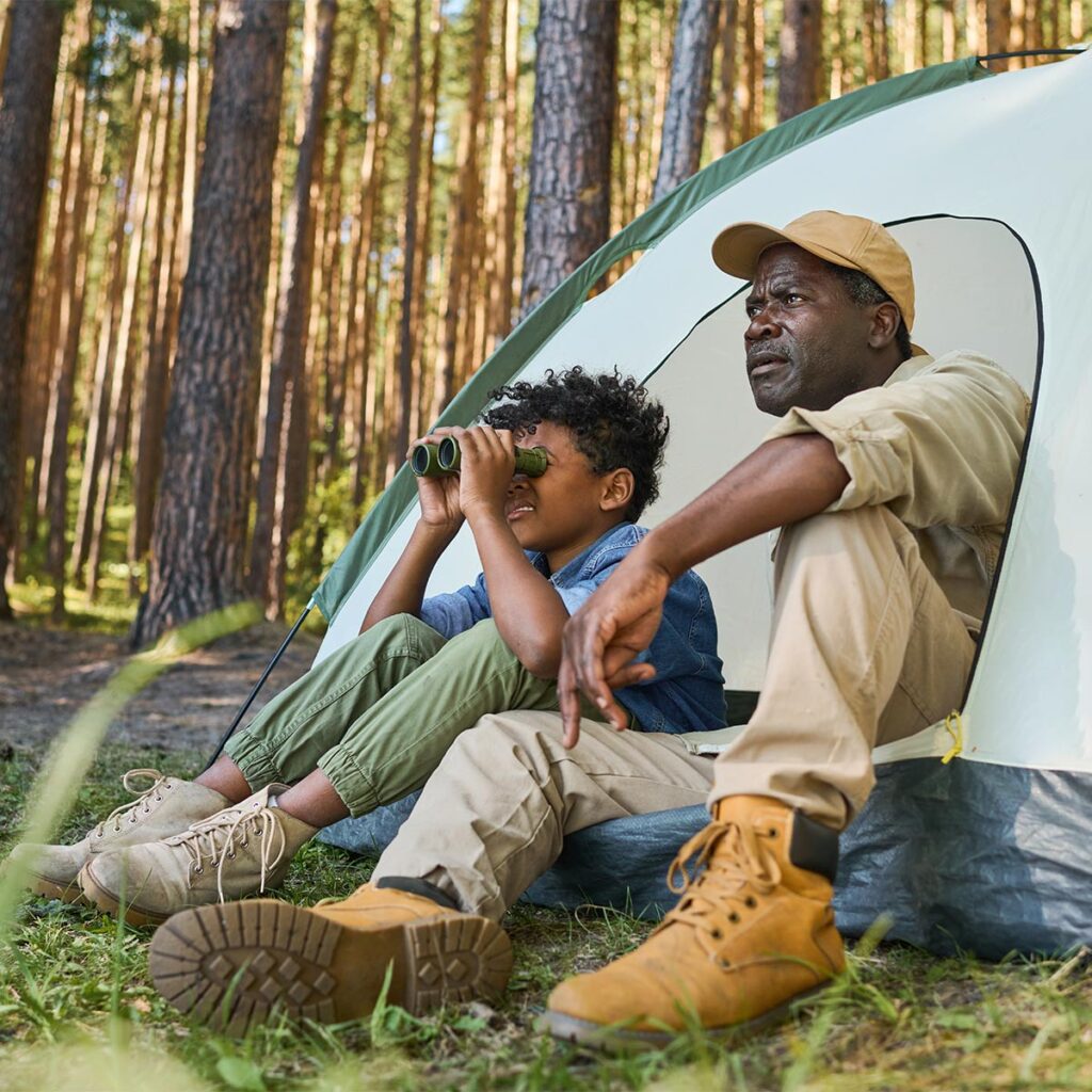 father and son looking out with binoculars in tent