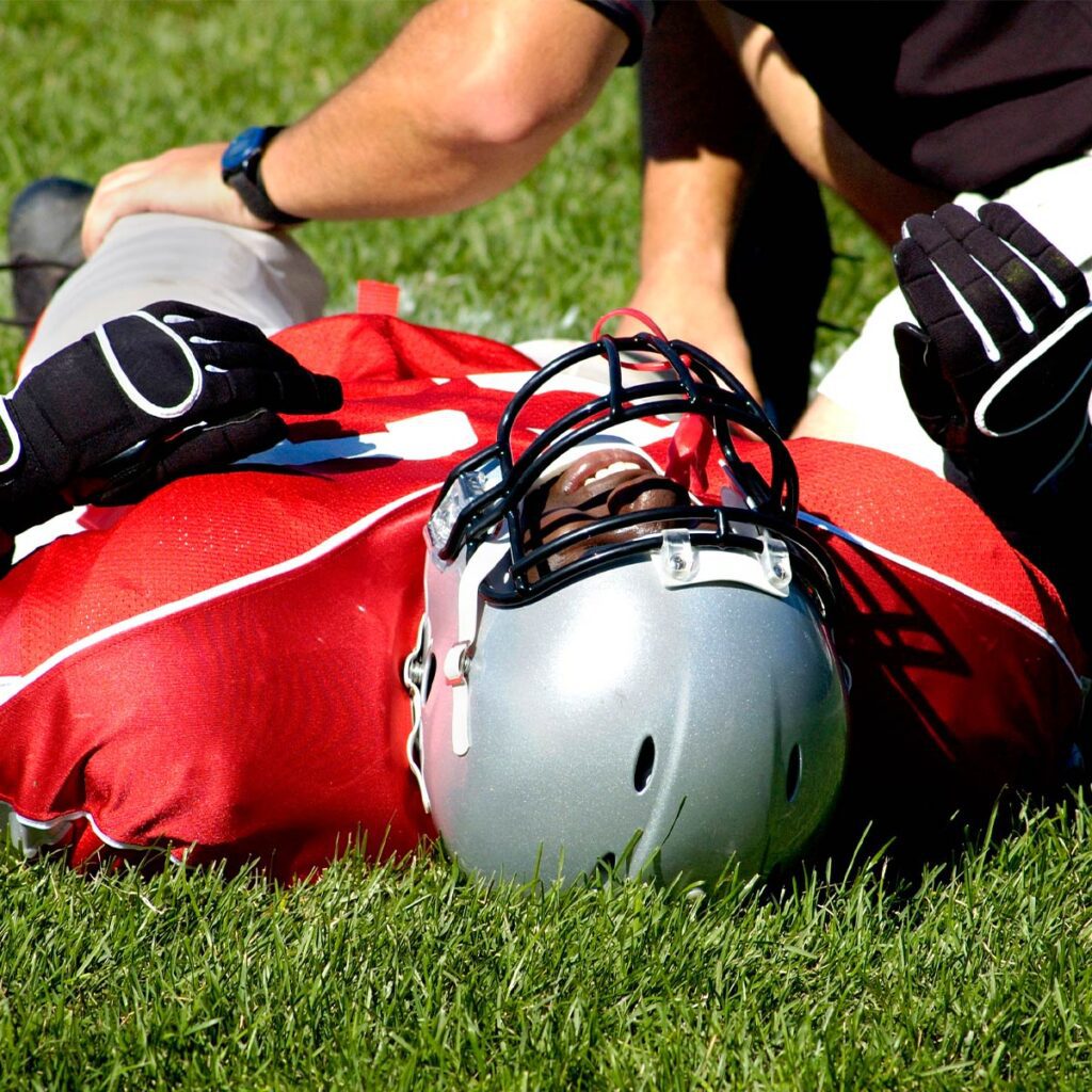injured football laying on grass while a coach looks at the injury