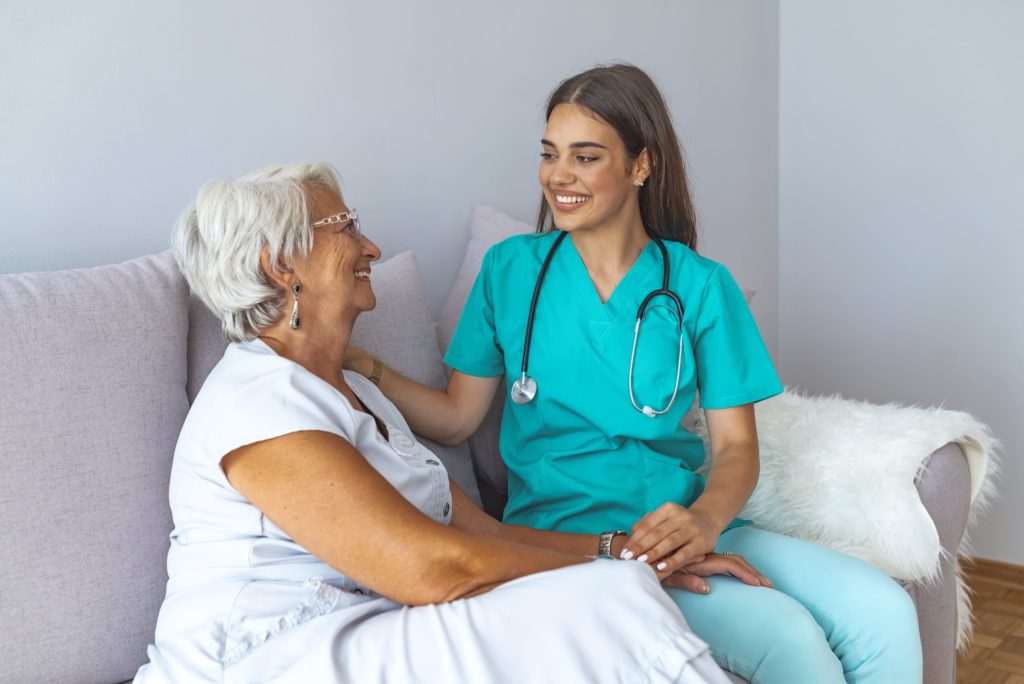 Happy patient is holding caregiver for a hand while spending time together. Elderly woman in nursing home and nurse. Aged elegant woman and tea time at nursing home