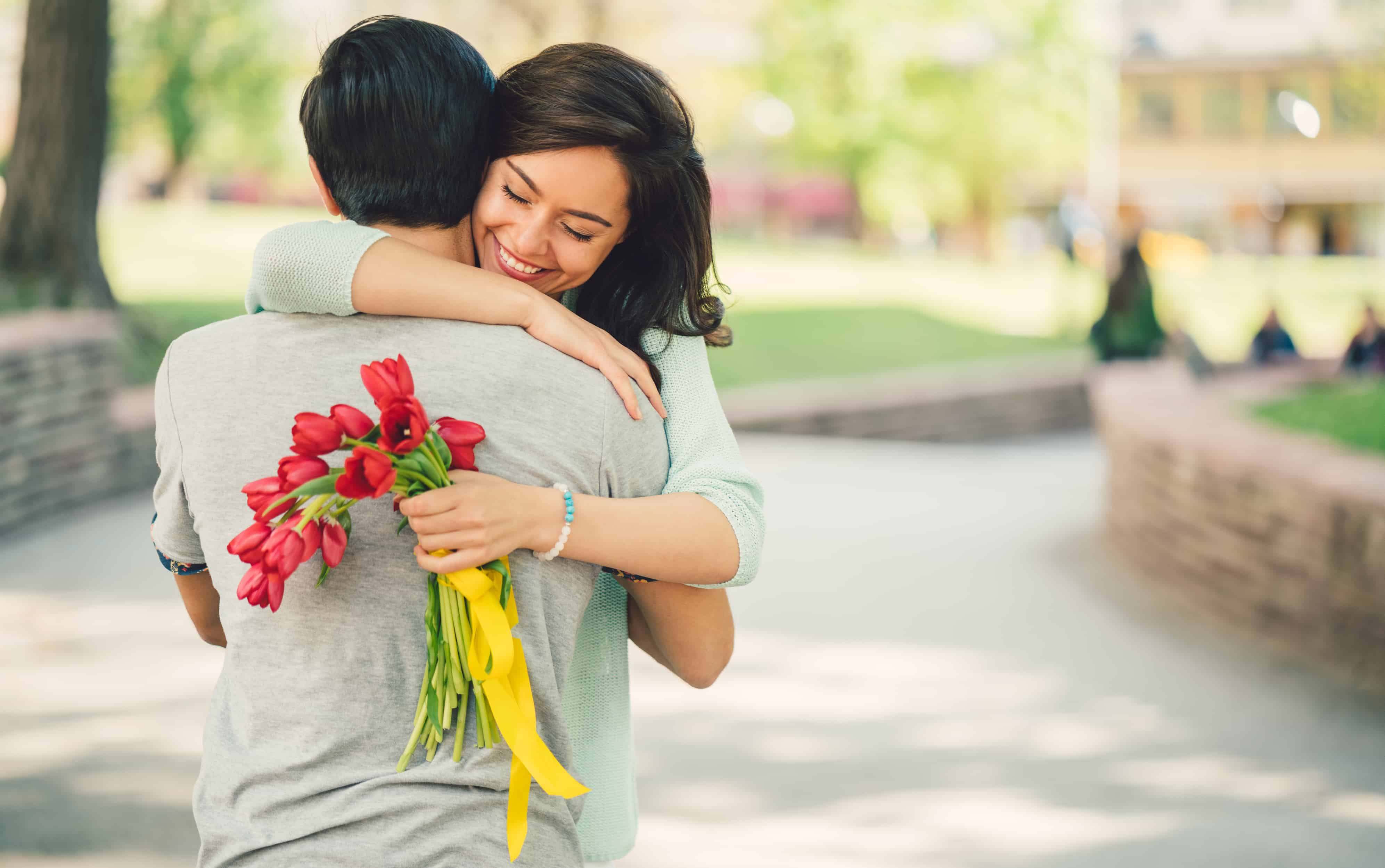Woman embraces man with flowers in her hand