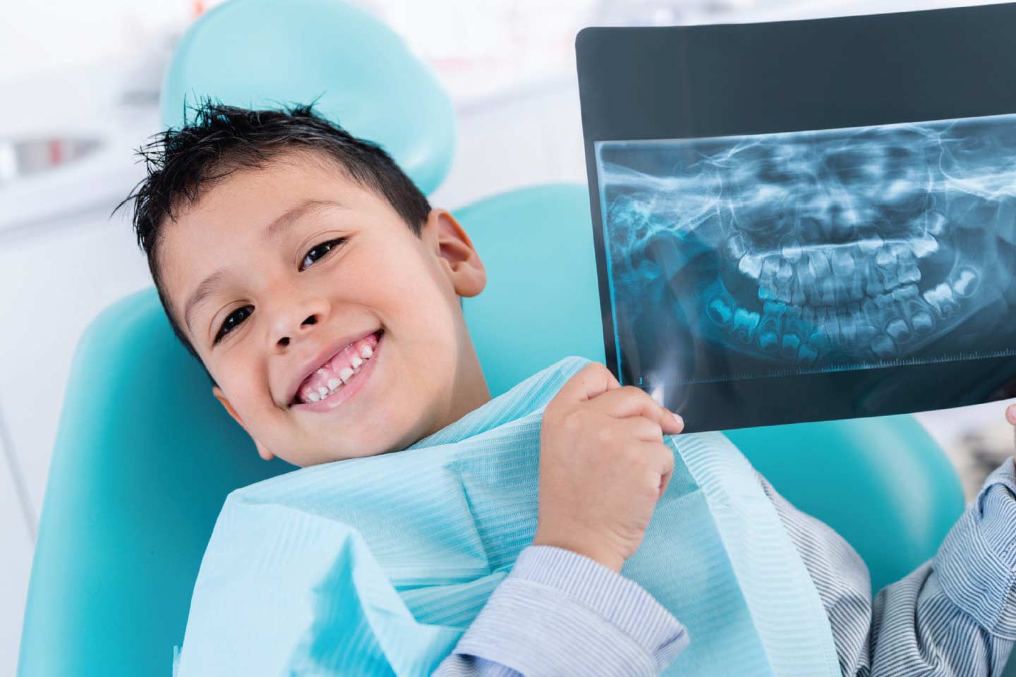 Kid smiling while holding up dental x-rays