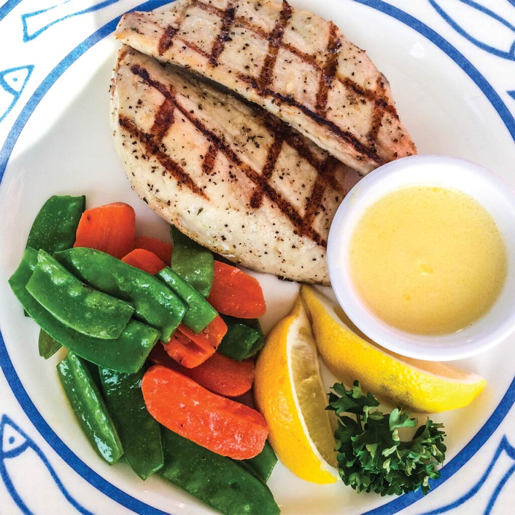 plate of grilled chicken with two lemon slices, sauce, and a portion of vegetables