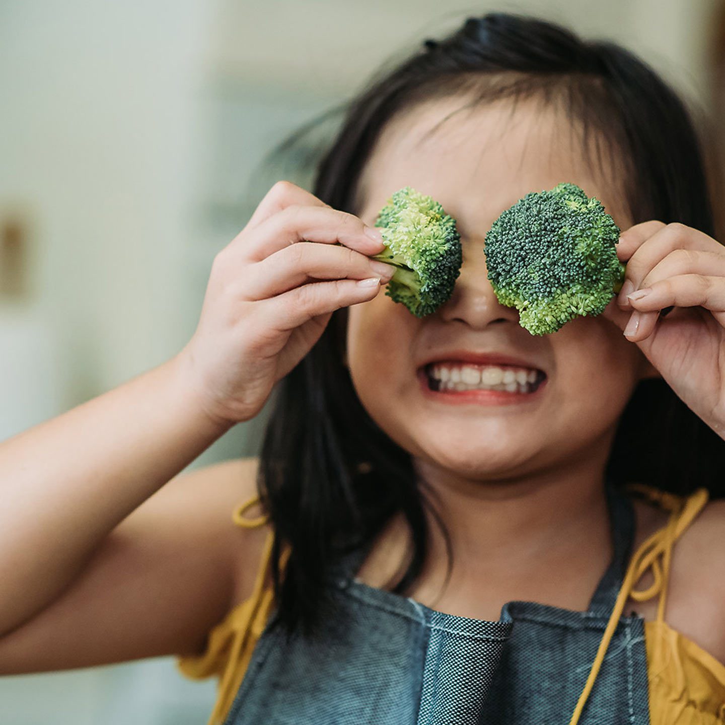 little girl holding broccoli over her eyes
