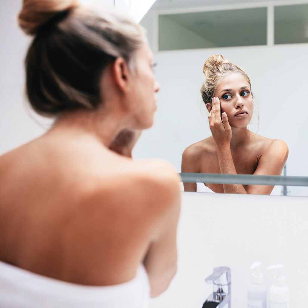 woman looking at her hyperpigmented face in the mirror