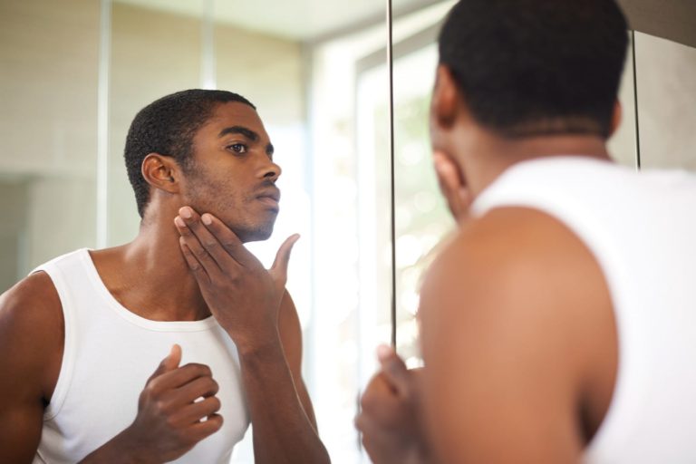 man looking in the mirror and applying aftershave