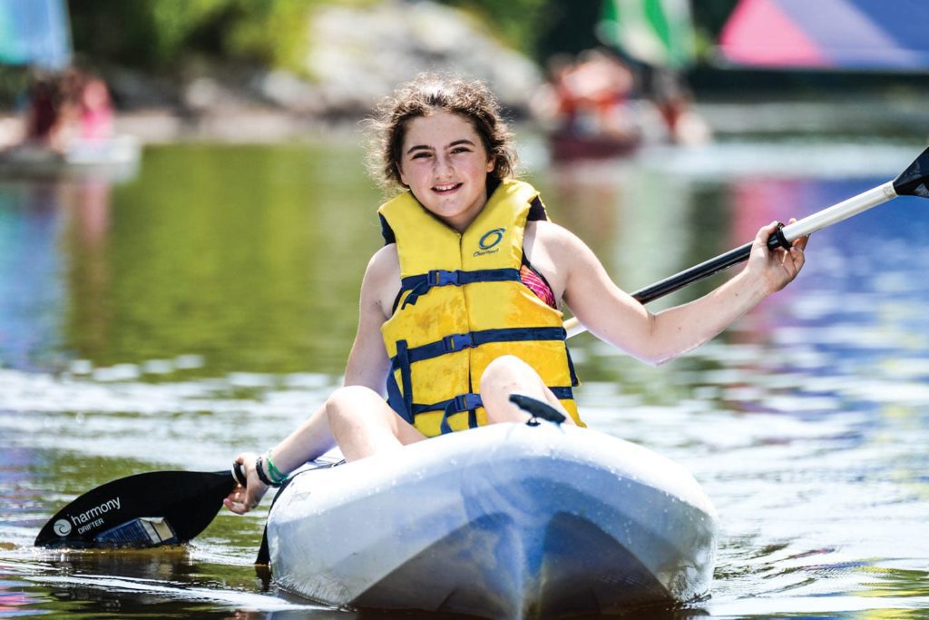 smiling girl paddling in a canoe at camp juliette low