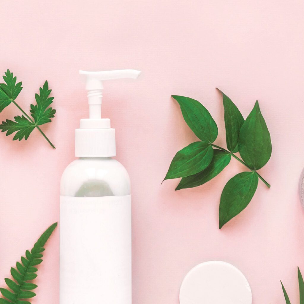 flat lay with skin care products and leaves on a pink background