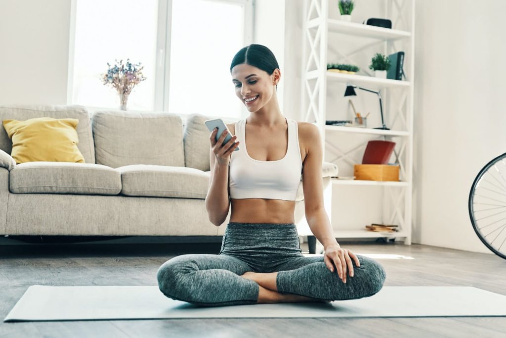 Woman sitting on yoga mat and looking at her phone