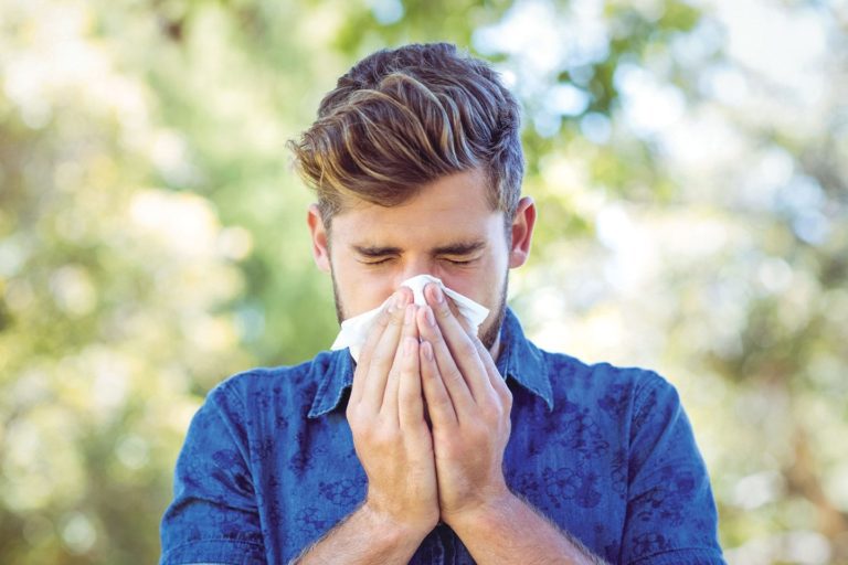 man sneezing outdoors because of allergies