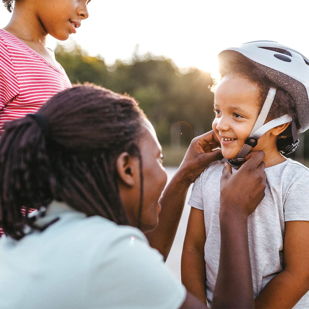 father adjusting his child's bicycle helmet while daughter watches
